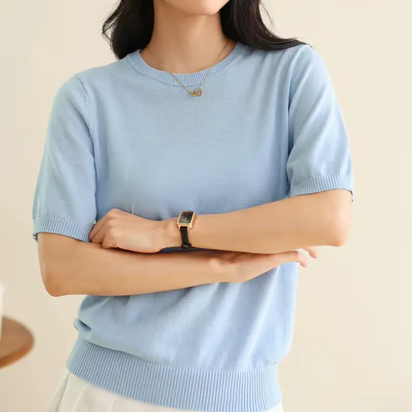 Person wearing a light blue sweater with arms crossed on a beige background
