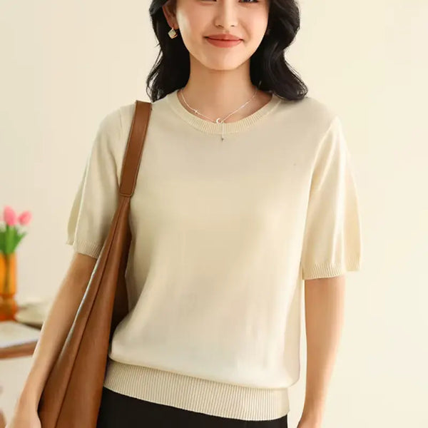 Woman wearing a light-colored sweater with a brown bag, standing against a neutral background.