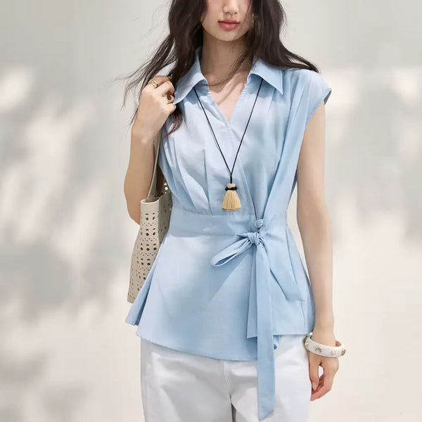 Woman wearing a light blue sleeveless top with a necklace against a neutral background