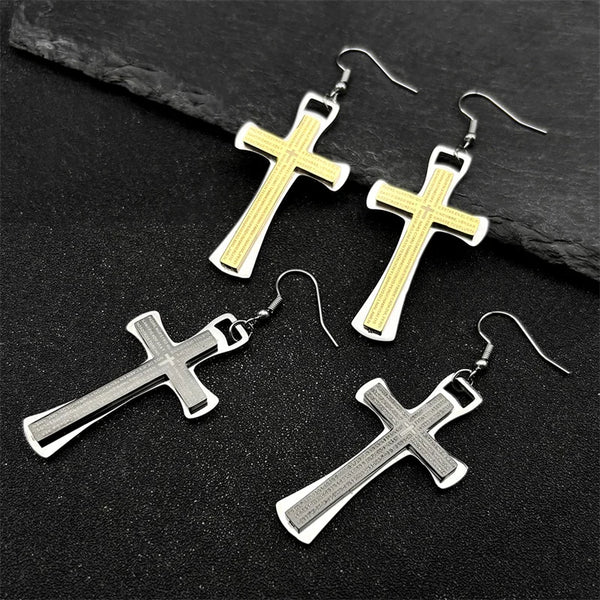 Cross-shaped earrings in gold and silver on a dark stone surface