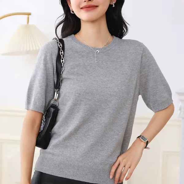 Woman wearing a gray sweater with a black handbag over her shoulder indoors.