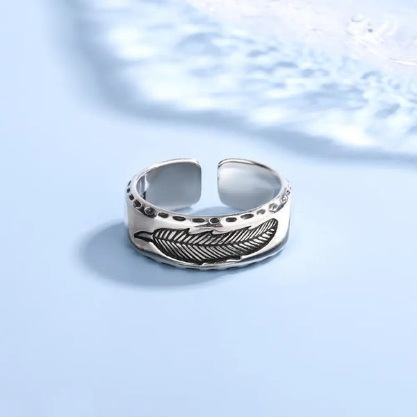 Silver ring with feather design on a light blue background