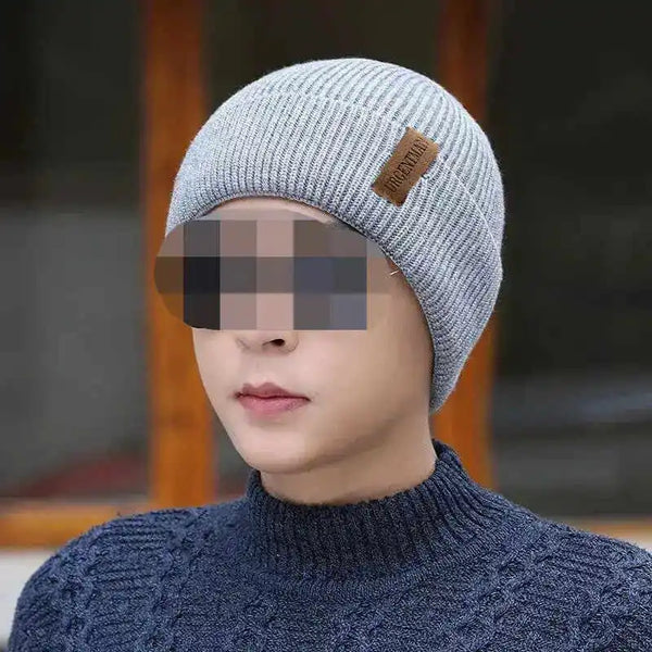 Person wearing a gray knit beanie with a brand logo, blurred face