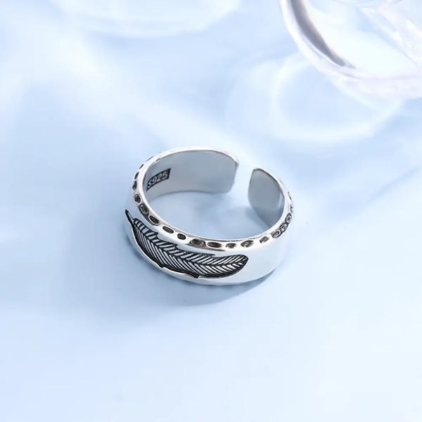 Silver ring with feather design on a light blue background