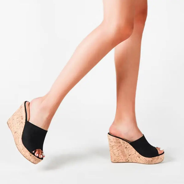 Black wedge sandals with cork soles worn by a person on a white background