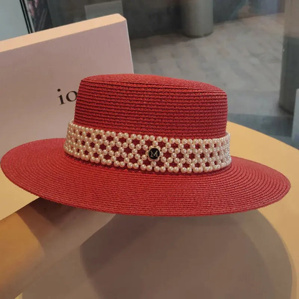Red straw hat with a pearl band on a reflective surface