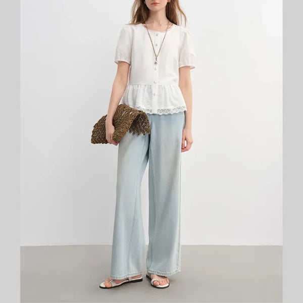 Woman wearing a white blouse and light blue pants holding a woven clutch against a plain background