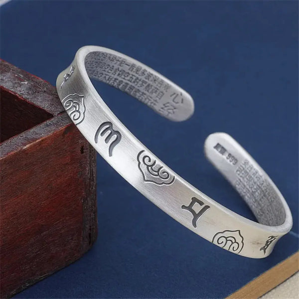 Silver bracelet with engraved symbols on a wooden box against a blue background