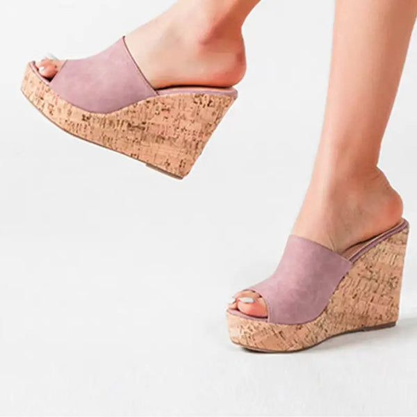 Pink wedge sandals with cork sole worn by a person on a light gray background