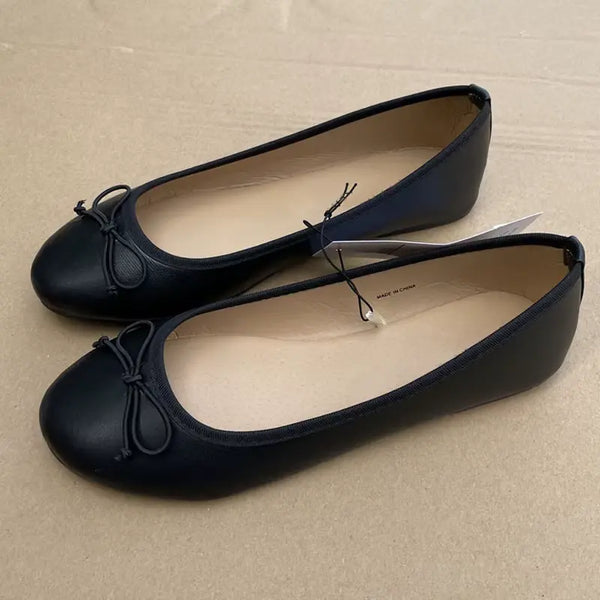 Pair of black ballet flats with a bow on a beige surface