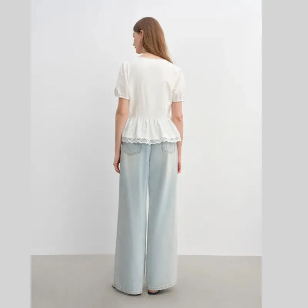 Woman wearing a white top and light blue pants against a plain background