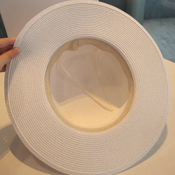 White straw hat held by a hand on a light surface
