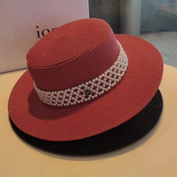 Red straw hat with pearl band on a beige surface