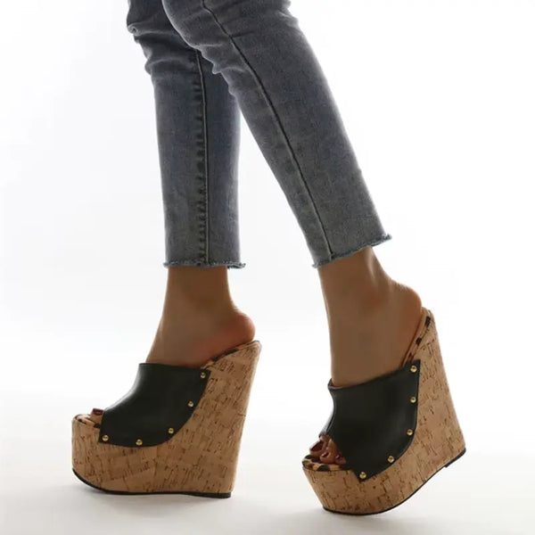 Wedges with cork sole and black leather straps worn with jeans on a white background