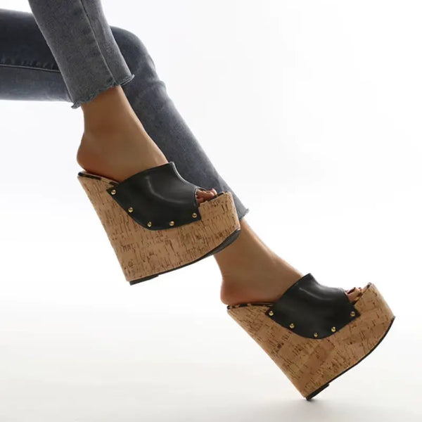 Black platform clogs with cork sole worn by a person on a white background