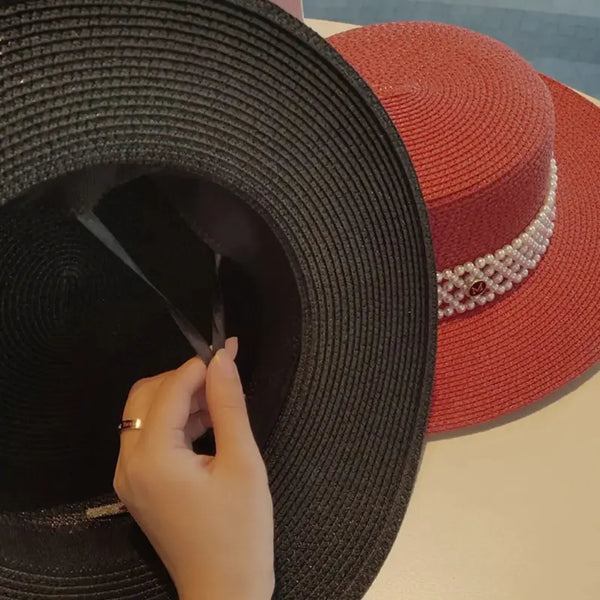Black and red straw hats with a hand adjusting the black hat on a light background