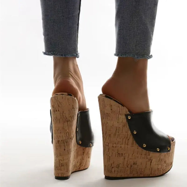 Wedges with cork sole and black leather accents worn with jeans on a white background