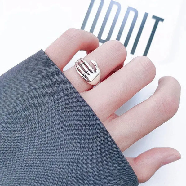 Hand wearing a gold ring with a hand design on a white background