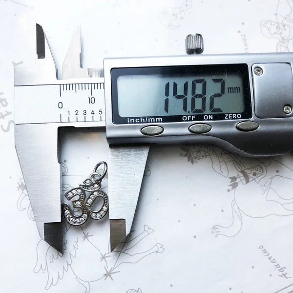 Digital caliper measuring a silver pendant on a white background with star constellations.