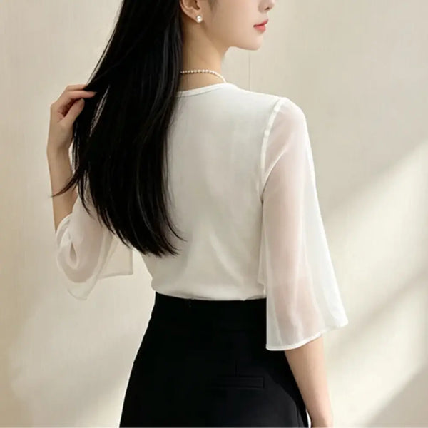 A woman shown from the back wearing a white sheer three-quarter sleeve blouse with a round neckline, paired with a black skirt, against a soft beige background.