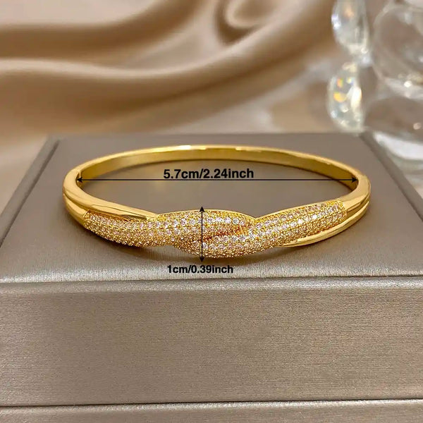 Gold bangle bracelet with pavé crystal detailing, displayed on a gray jewelry box with overlaid dimension markers showing 5.7 cm width and 1 cm height.