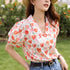 Woman wearing a floral blouse with heart patterns outdoors.
