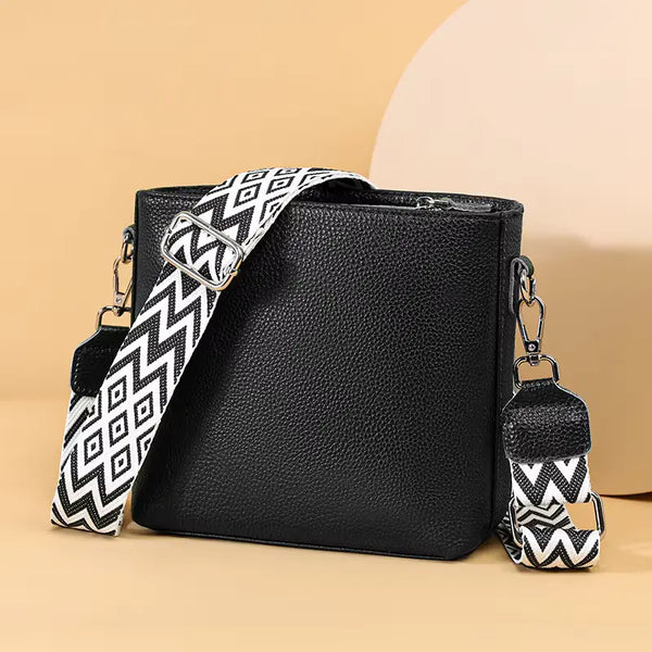 Black leather handbag with a patterned strap and keychain on a beige background
