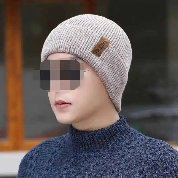 Person wearing a beige knit beanie with a brand logo, blurred background