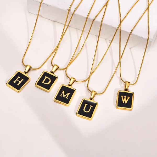 Gold necklaces with black square pendants displaying letters on a white background