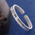 Silver bracelet with engraved symbols on a blue background