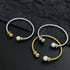 Two twisted cable cuff bracelets displayed on a dark textured background. One bracelet is silver-toned with a gold bead and white pearl, and the other is gold-toned with a silver bead and white pearl.