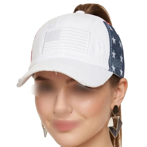 A woman wearing a white distressed baseball cap with a white embroidered American flag on the front and a navy blue mesh side panel decorated with white stars.