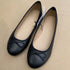 Pair of black flat shoes with bow details on a beige background