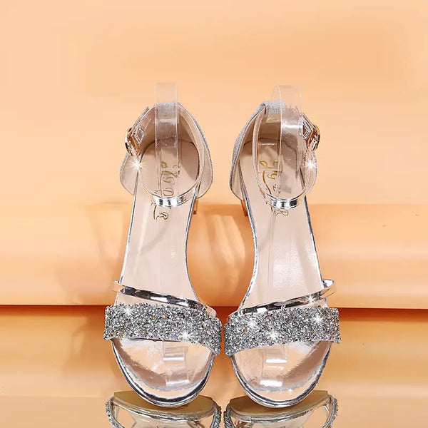 Silver high-heeled sandals with glittery straps on a reflective surface.