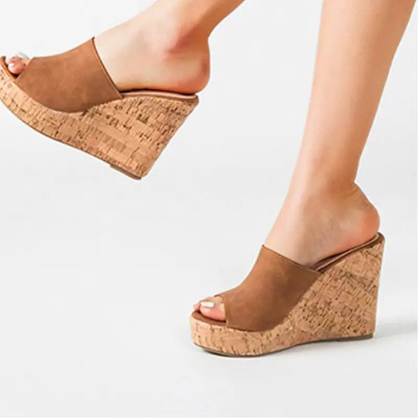 Brown wedge sandals with cork sole worn by a person on a light gray background