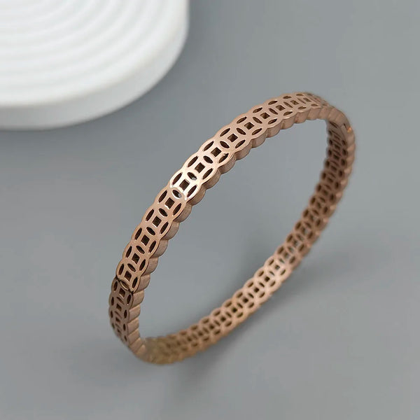 Rose gold bracelet with intricate pattern on a gray background