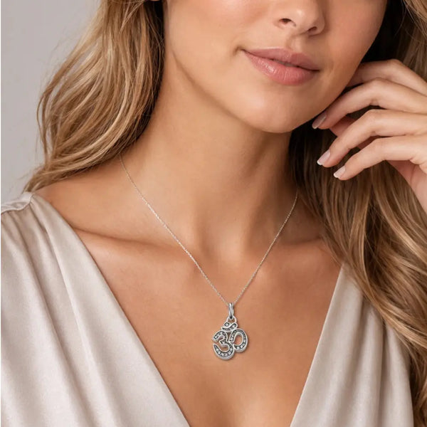 A close-up lifestyle shot of a woman wearing a delicate silver Om pendant necklace with a fine beaded chain, styled with a beige satin top.