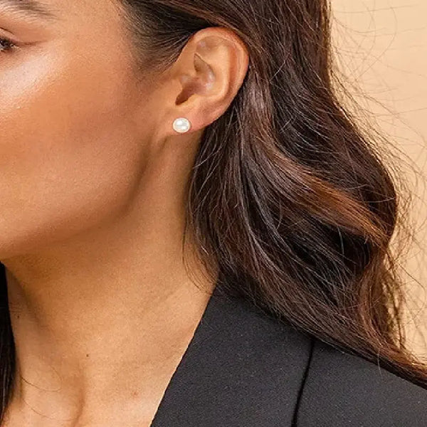 Close-up of a person wearing a pearl stud earring with a neutral background