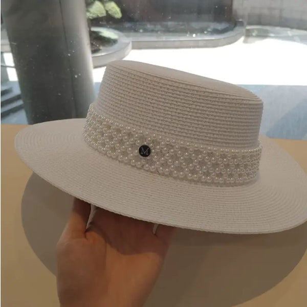 White straw hat with a pearl band held by a hand on a light surface.