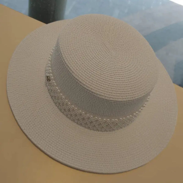 Beige straw hat with pearl embellishments on a reflective surface