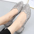Silver floral embellished shoes worn by a person on a light gray background