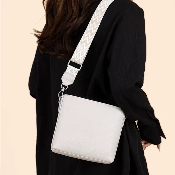 White crossbody bag worn by a person in a black outfit on a beige background