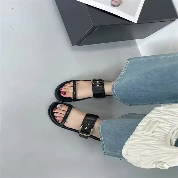 Black sandals worn with blue jeans on a light gray floor.