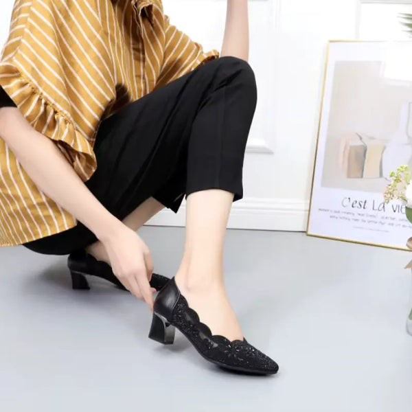 Person wearing black shoes with a decorative pattern, sitting on a light-colored floor.